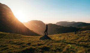 Photographie De Silhouette De Personne Debout Sur L'herbe Verte En Face De Montagnes Pendant L'heure D'or