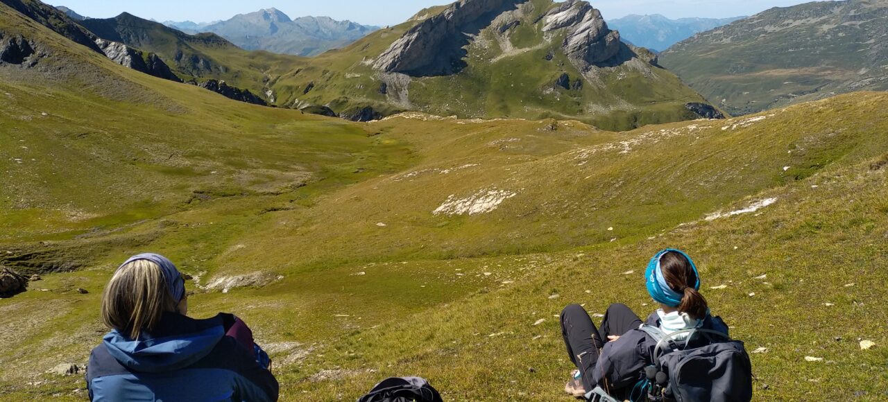 randonneurs faisant une pause dans l'herbe, et contemplant le rocher du Vent (Beaufortain)